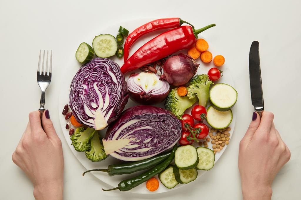 Обрезанный вид женщины со столовыми приборами и свежими овощами
  - Фото, изображение