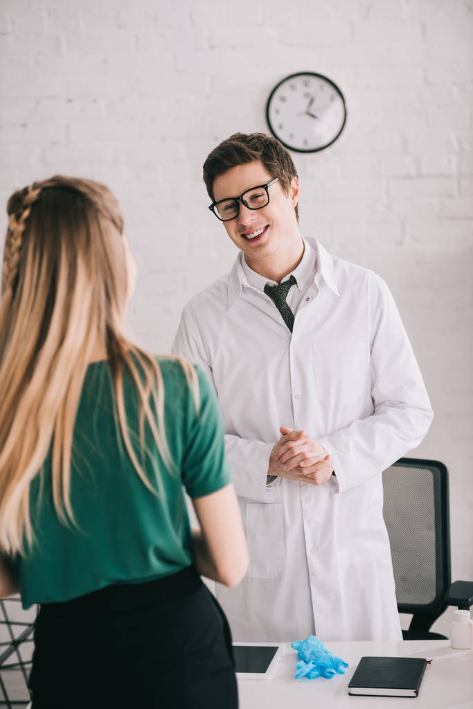 Rückansicht einer Frau, die in Brille und weißem Mantel neben einem Arzt steht  - Foto, Bild