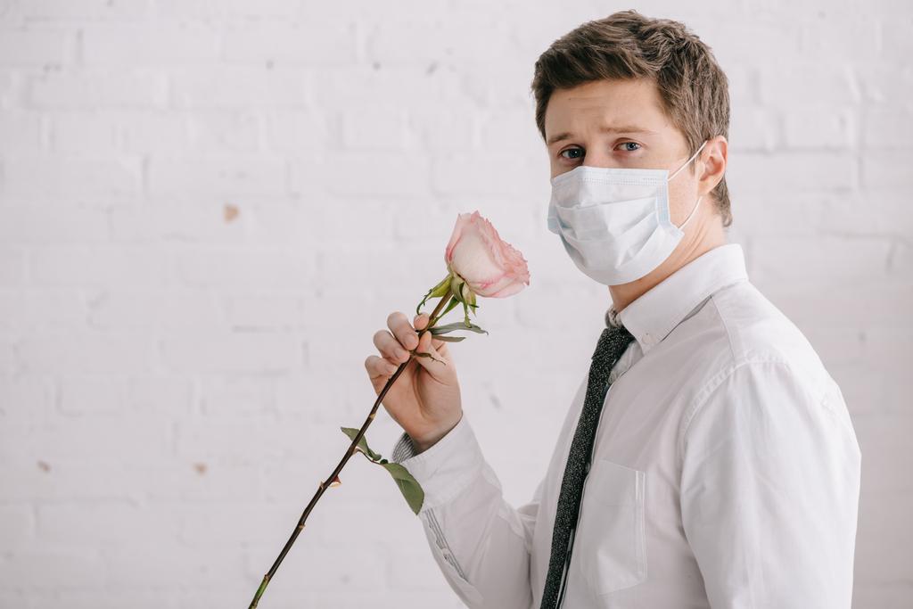 ο άνθρωπος στην ιατρική μάσκα κρατώντας τριαντάφυλλο και βλέπουν τα φωτογραφικών μηχανών  - Φωτογραφία, εικόνα