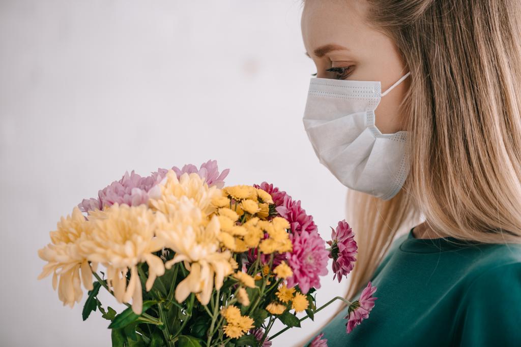 femme blonde allergique au pollen portant un masque médical et regardant un bouquet de fleurs
  - Photo, image
