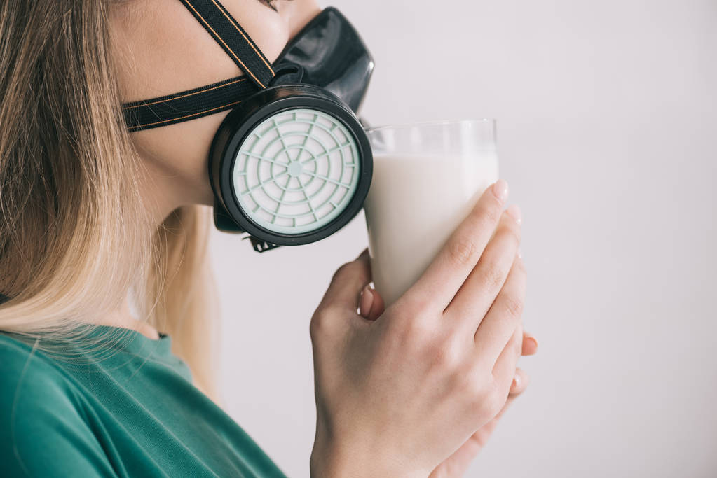 bijgesneden weergave van blonde vrouw in respiratoire masker melk ruiken terwijl glas - Foto, afbeelding