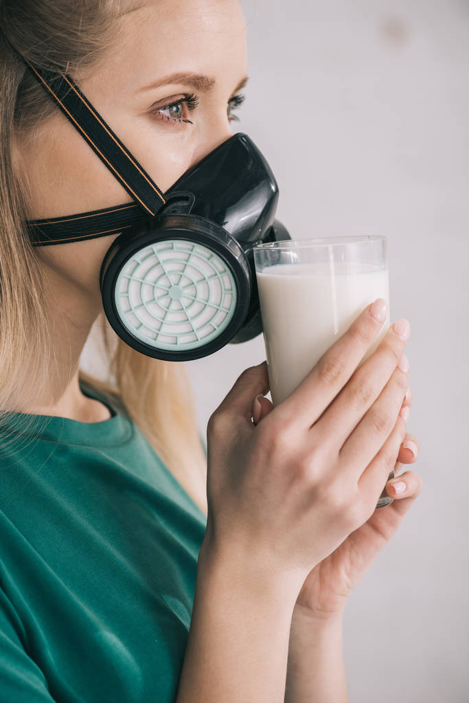 blonde woman in respiratory mask smelling milk while holding glass - Photo, Image