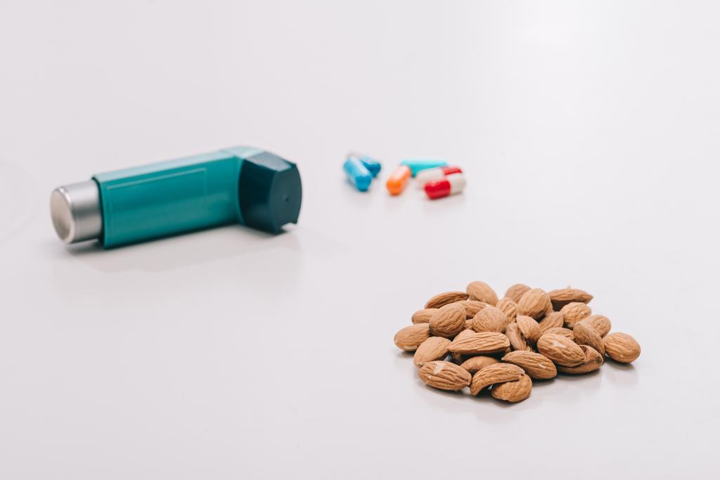 concentrazione selettiva di gustose mandorle vicino alle pillole e inalatore blu sul grigio
 - Foto, immagini