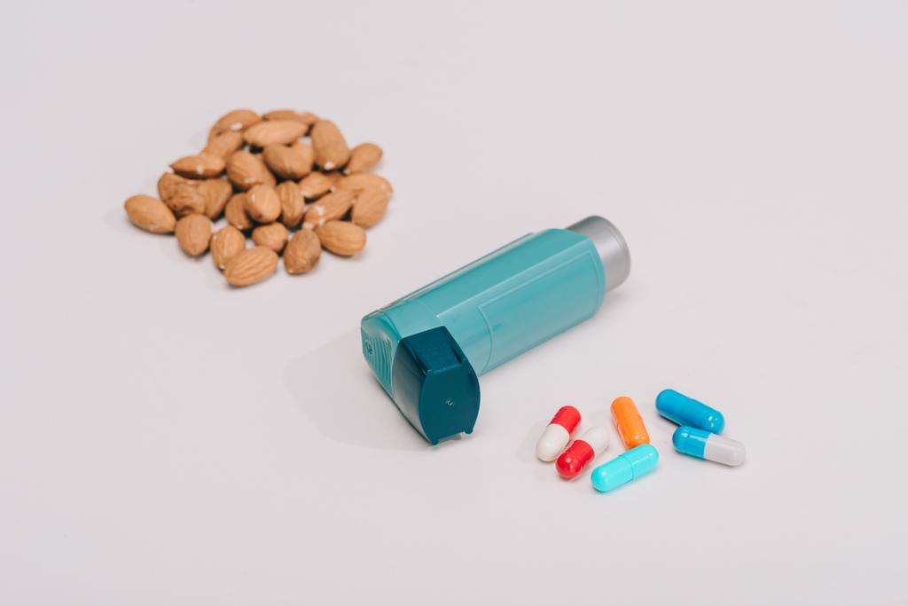 επιλεκτική εστίαση χάπια και μπλε συσκευή εισπνοής και γευστικά αμύγδαλα κοντά σε γκρι - Φωτογραφία, εικόνα