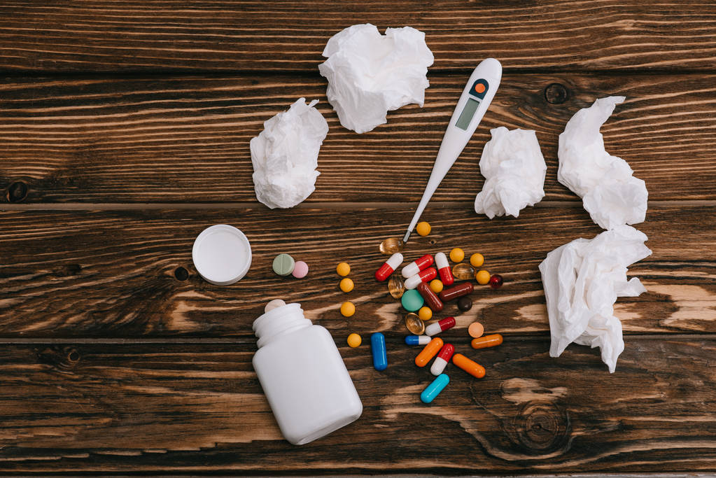 top view of white tissues near thermometer, bottle and pills on wooden surface  - Photo, Image