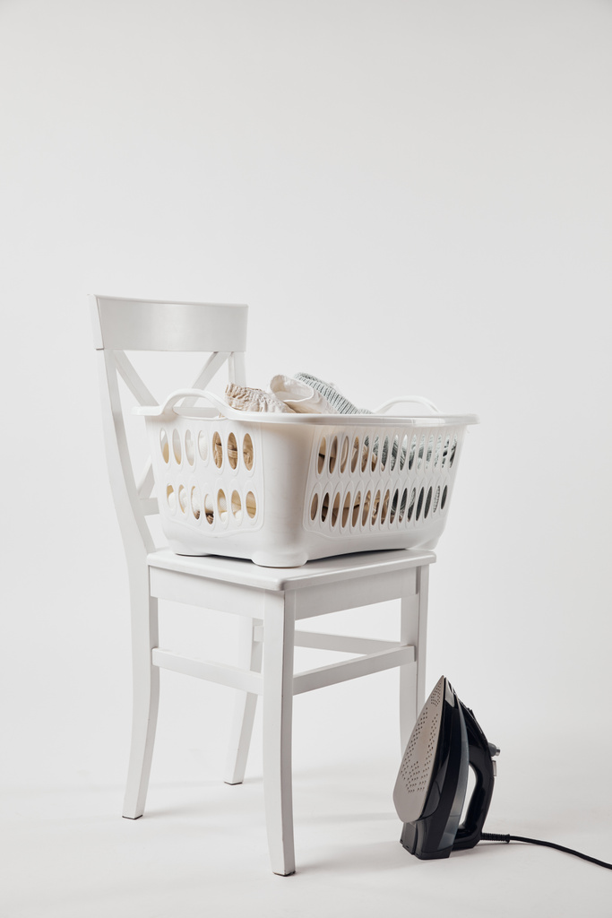 Bílá židle, koš na prádlo s oblečením a žehličkou na šedé - Fotografie, Obrázek