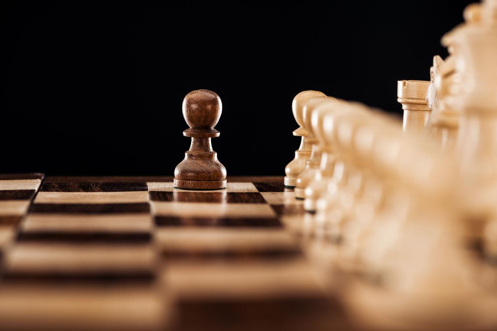 επιλεκτική εστίαση του ξύλινη σκακιέρα με ΦΙΓΟΥΡΕΣ ΣΚΑΚΙΟΥ και απομονώνονται μπροστά σε μαύρο πιόνι  - Φωτογραφία, εικόνα
