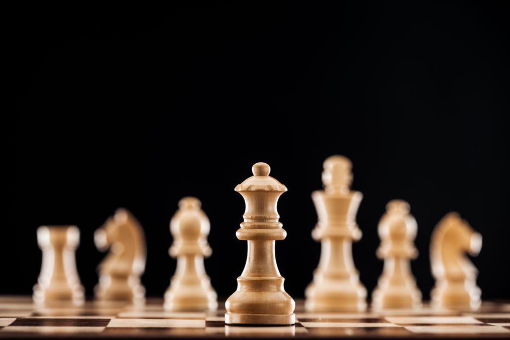 selective focus of beige wooden queen on chessboard isolated on black  - Photo, Image