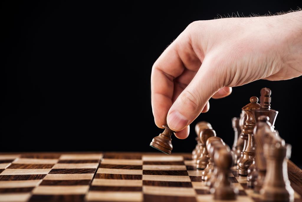 partial view of man doing move on wooden chessboard isolated on black - Photo, Image