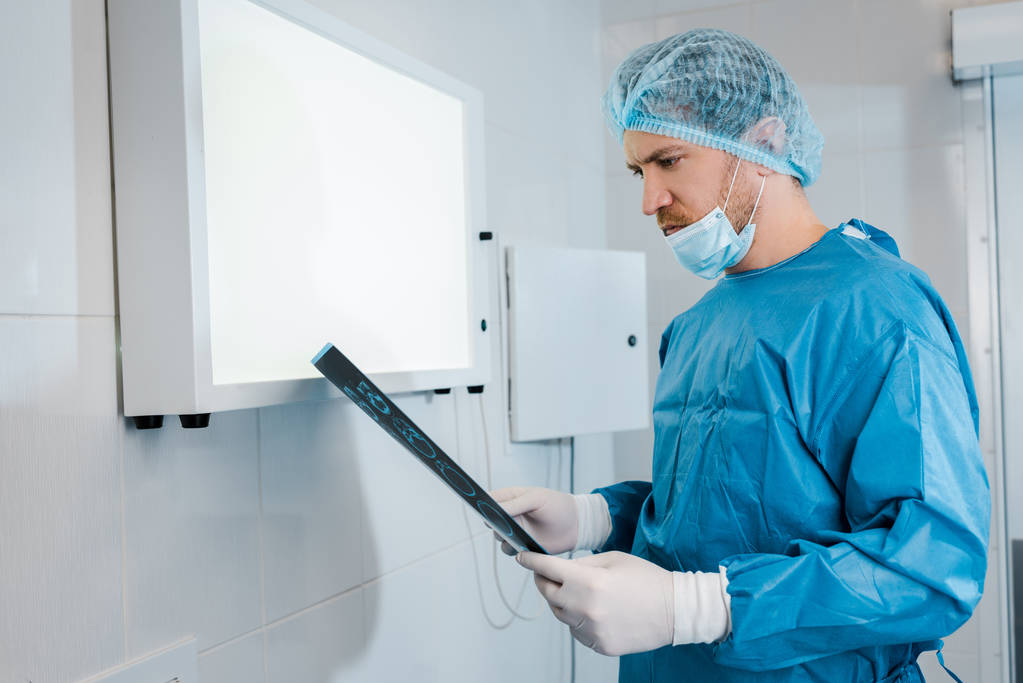 goed uitziende arts in de medische Cap en uniform Holding x-ray in de kliniek  - Foto, afbeelding