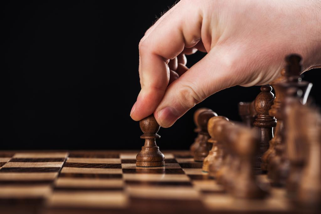bijgesneden beeld van de mens doet zet met pion op houten schaakbord geïsoleerd op zwart - Foto, afbeelding