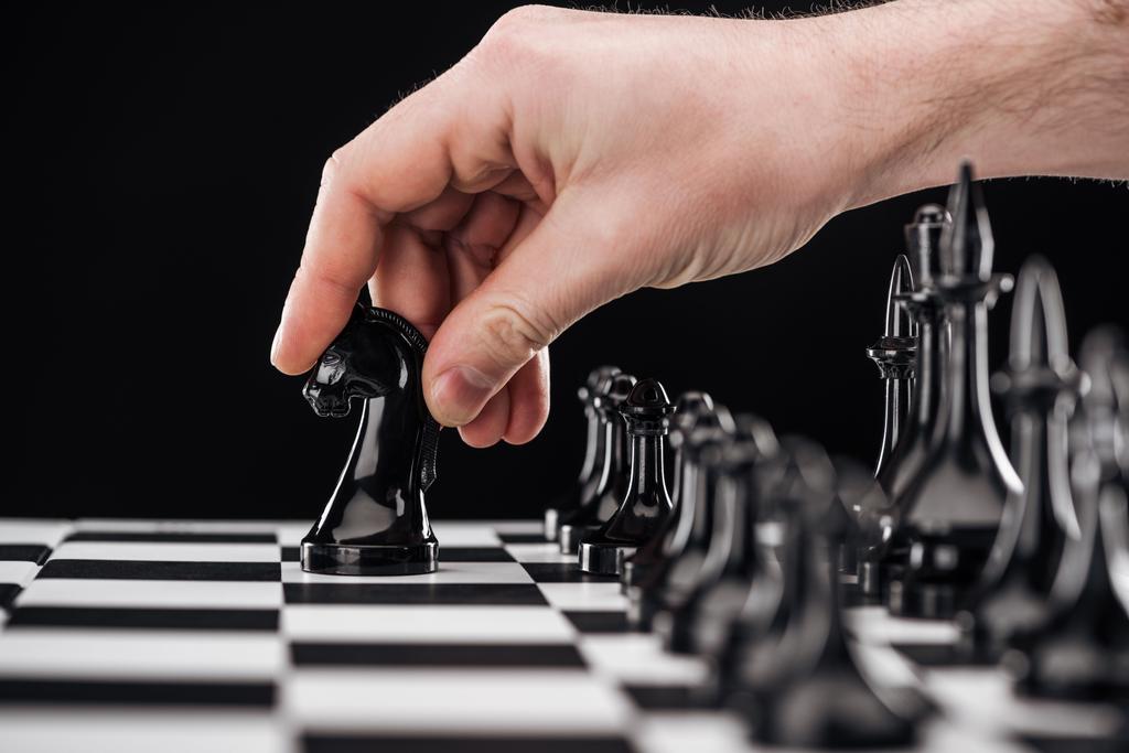 visão cortada do homem fazendo movimento com cavaleiro no tabuleiro de xadrez isolado no preto
 - Foto, Imagem