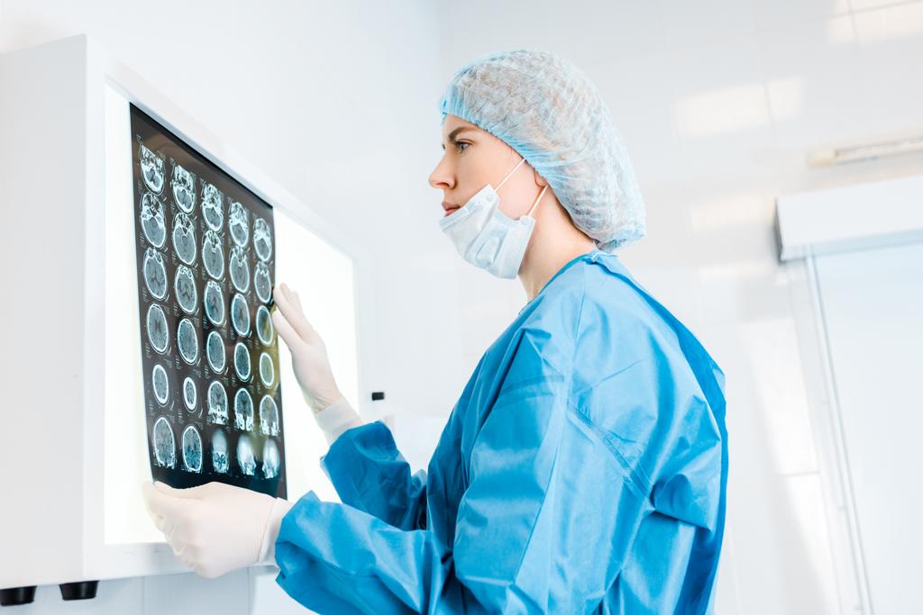 Seitenansicht des attraktiven Arztes in Mütze und Uniform mit Röntgenaufnahme in der Klinik  - Foto, Bild