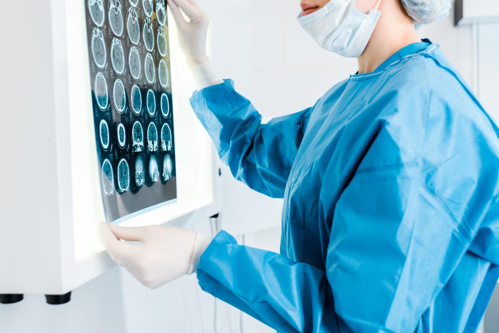 Ausgeschnittene Ansicht des Arztes in Mütze und Uniform mit Röntgenaufnahme in der Klinik  - Foto, Bild
