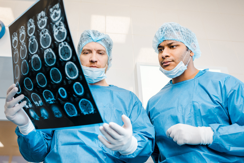 knappe artsen in uniformen en medische maskers praten over x-ray in de kliniek  - Foto, afbeelding
