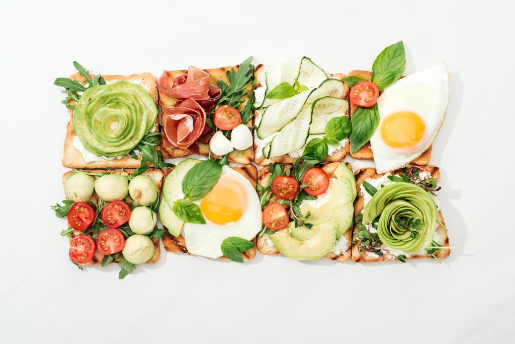 Vista superior de tostadas con verduras cortadas y jamón sobre superficie blanca
 - Foto, Imagen