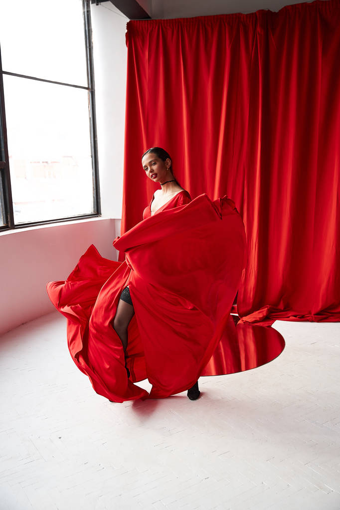 Sexy brunetka žena v dlouhé červené šaty, taneční Studio s velkými okny a červenými závěsy. - Fotografie, Obrázek