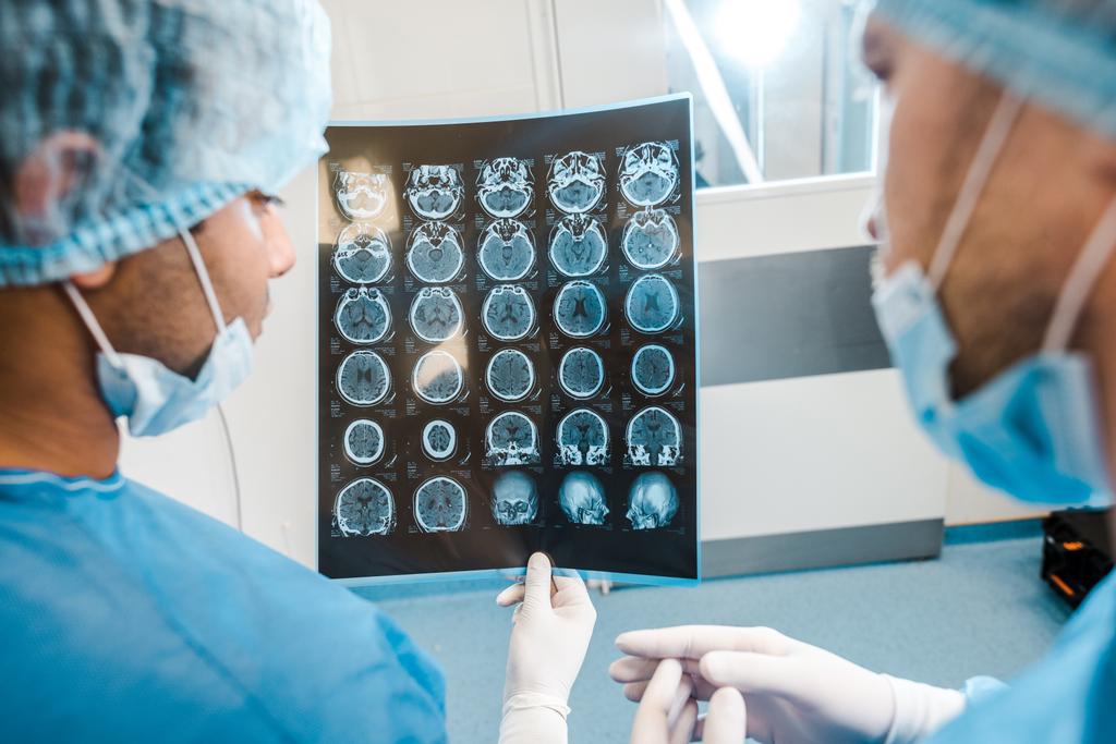 vista posterior de los médicos en uniformes y máscaras médicas mirando rayos X
 - Foto, Imagen