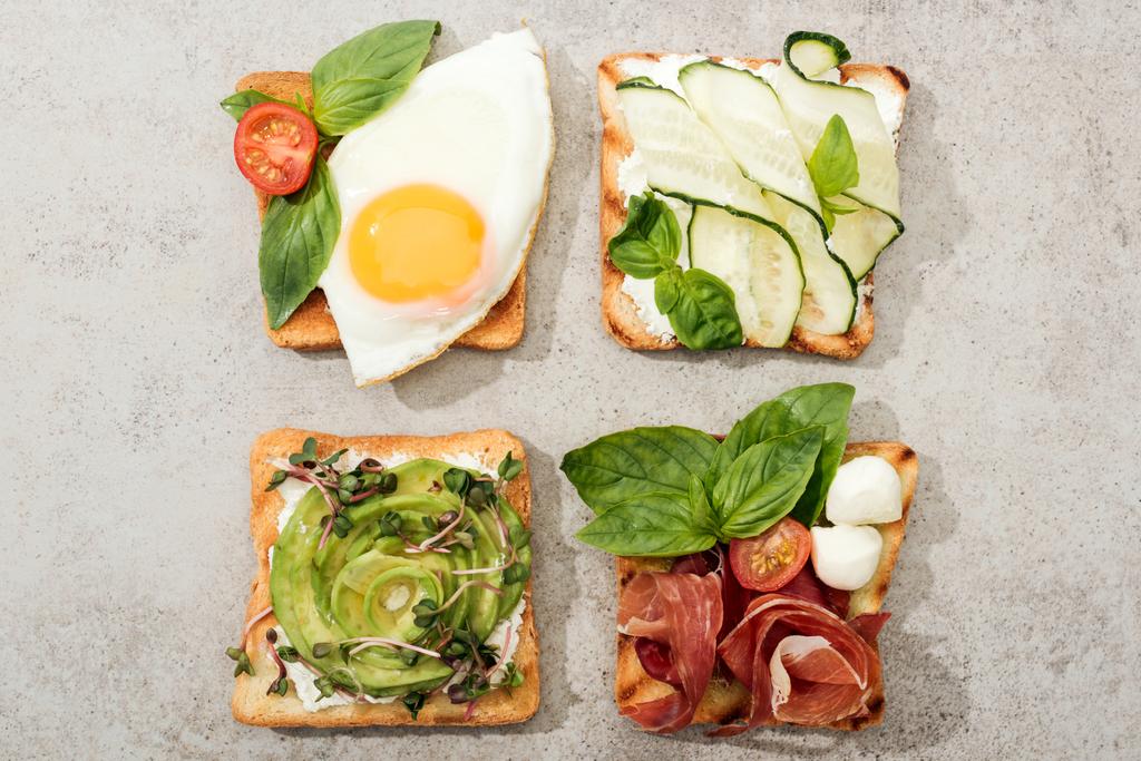 Top view of toasts with vegetables, fried egg and prosciutto on textured surface - Photo, Image