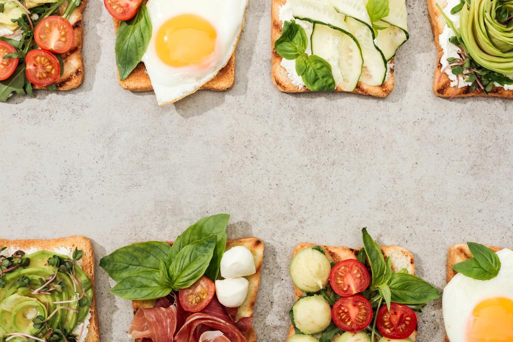 Top view of toasts with vegetables, fried eggs and prosciutto on textured surface - Photo, Image
