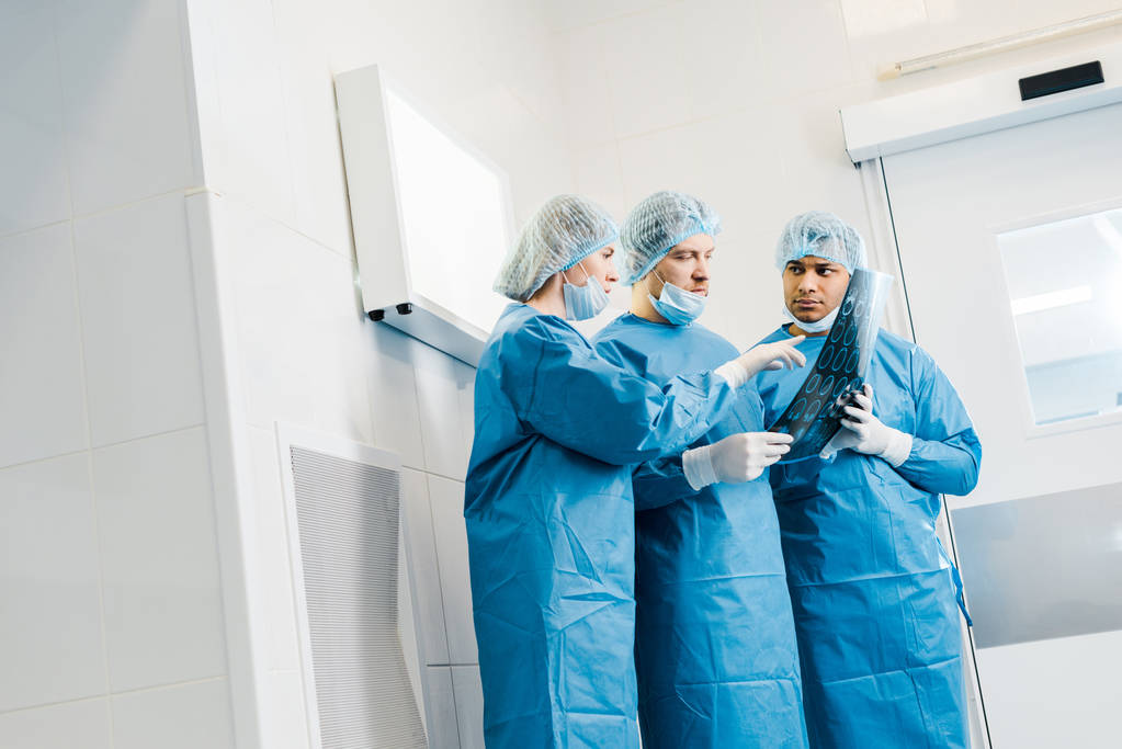 médicos bonitos e atraentes em uniformes e máscaras médicas apontando com o dedo para o raio-x e falando
 - Foto, Imagem