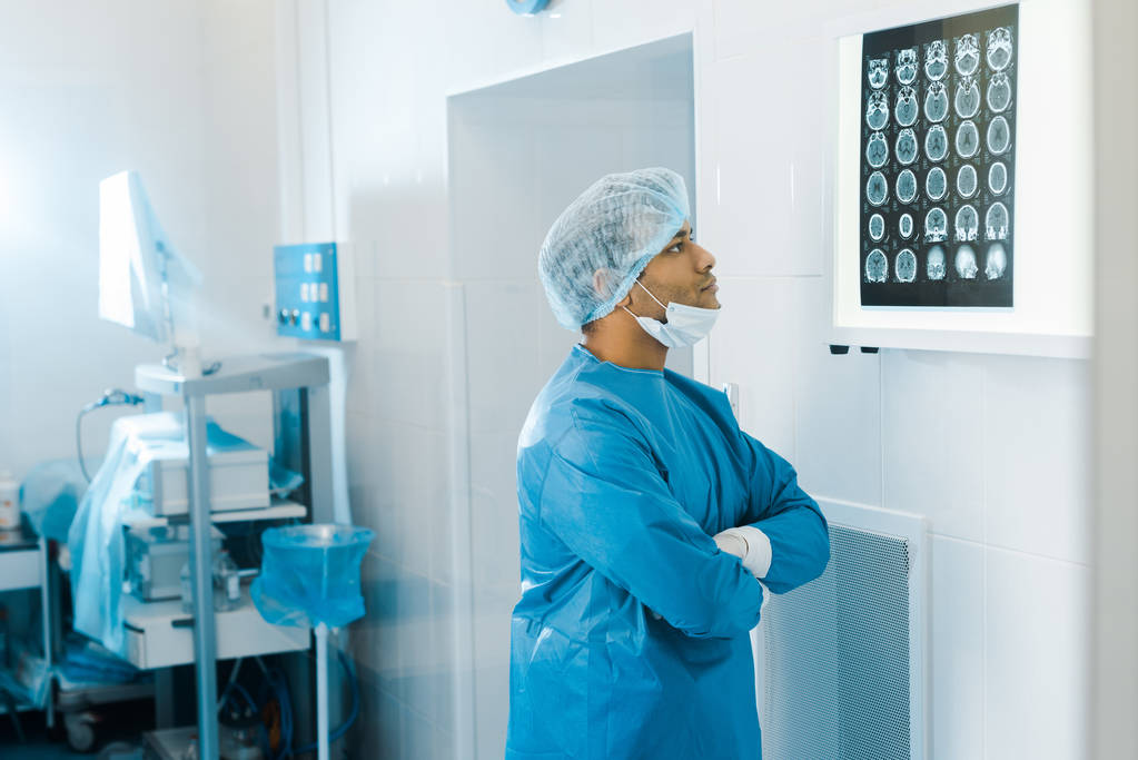 medico in uniforme e maschera medica con braccia incrociate guardando i raggi X
  - Foto, immagini