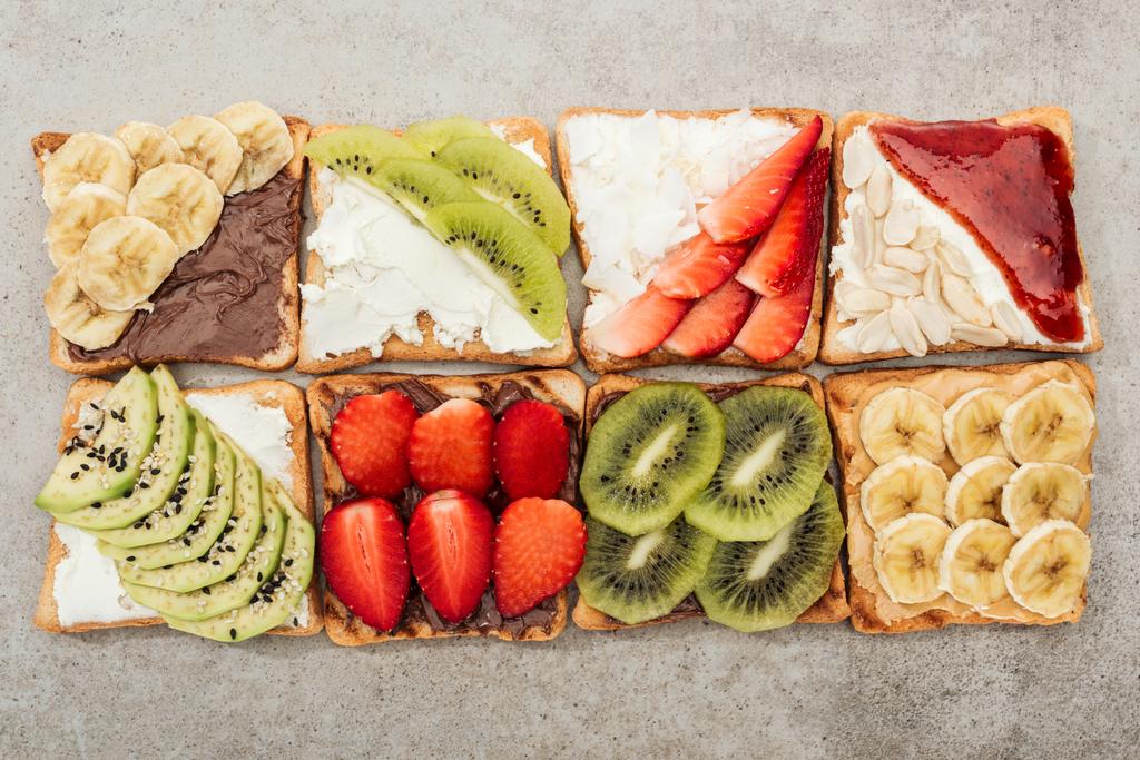 Vista superior de torradas com frutas cortadas, bagas e amendoins na superfície texturizada
 - Foto, Imagem