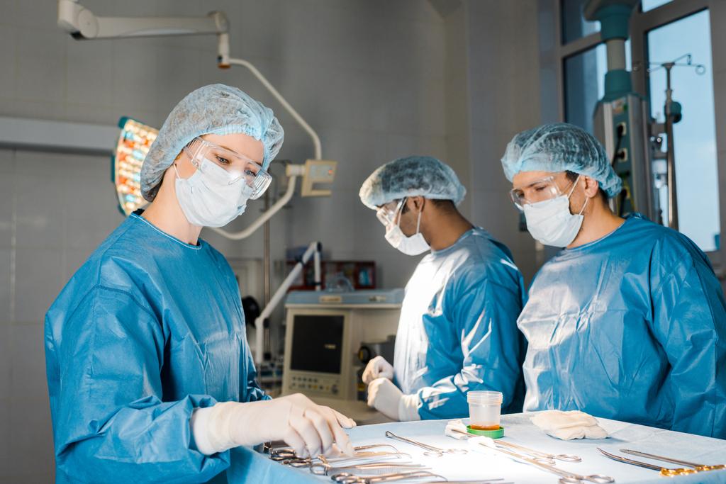 doctors doing operation and nurse in uniform and medical cap giving equipment  - Photo, Image