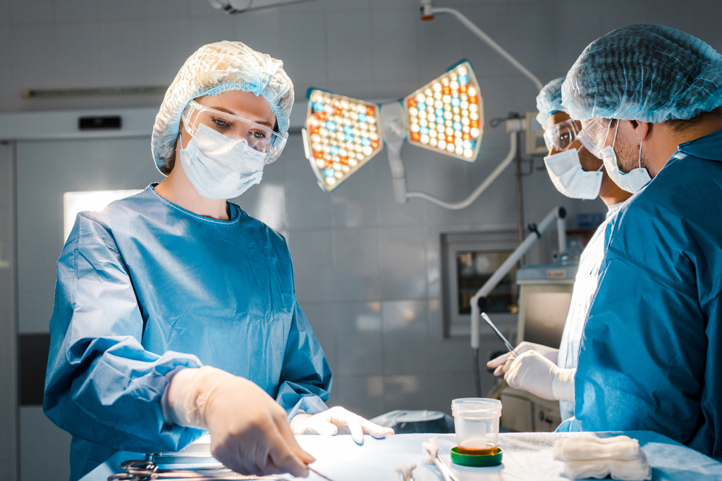 νοσηλευτή κρατώντας εξοπλισμό και γιατρούς σε στολές και ιατρικά καπάκια στο χειρουργείο - Φωτογραφία, εικόνα