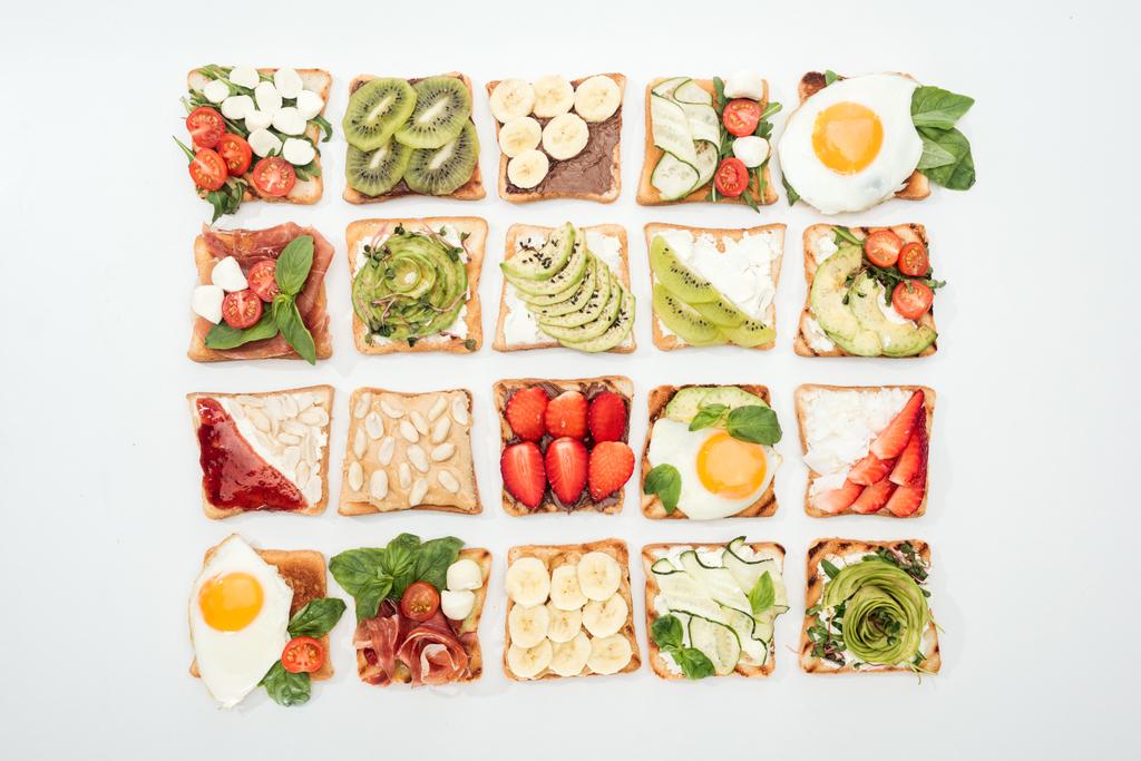 Top view of toasts with cut fruits, vegetables and peanuts on white - Photo, Image