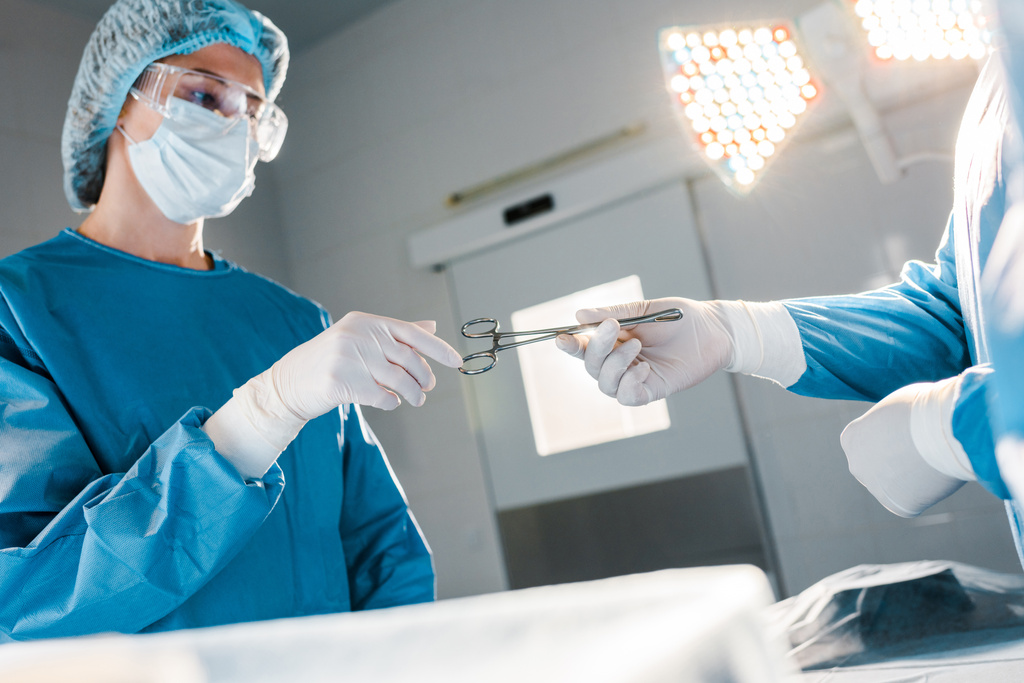 Arzt gibt Krankenschwester in Uniform und medizinischer Maske medizinisches Gerät  - Foto, Bild