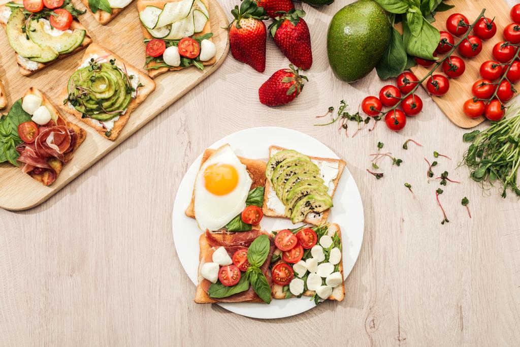 верхний вид ингредиентов и тостов с овощами, яичницей и прошутто на деревянном столе
 - Фото, изображение