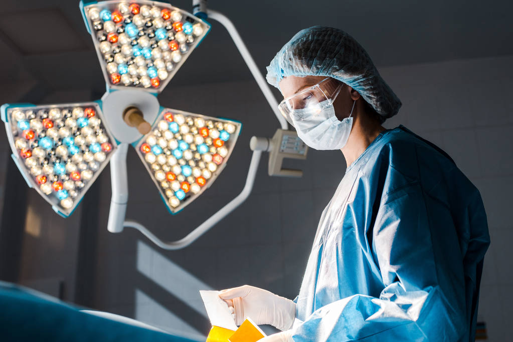 enfermeira em uniforme e tampa médica segurando tira na sala de cirurgia
  - Foto, Imagem