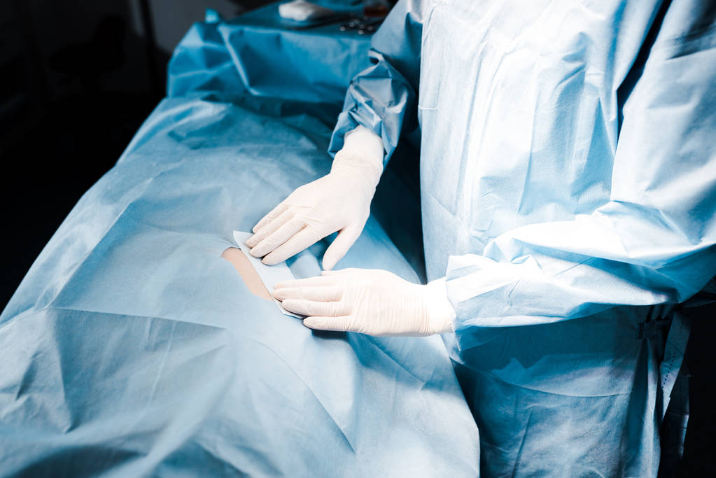 częściowy widok pielęgniarki w mundurach i rękawice lateksowe zakładanie taśmy w sali operacyjnej - Zdjęcie, obraz