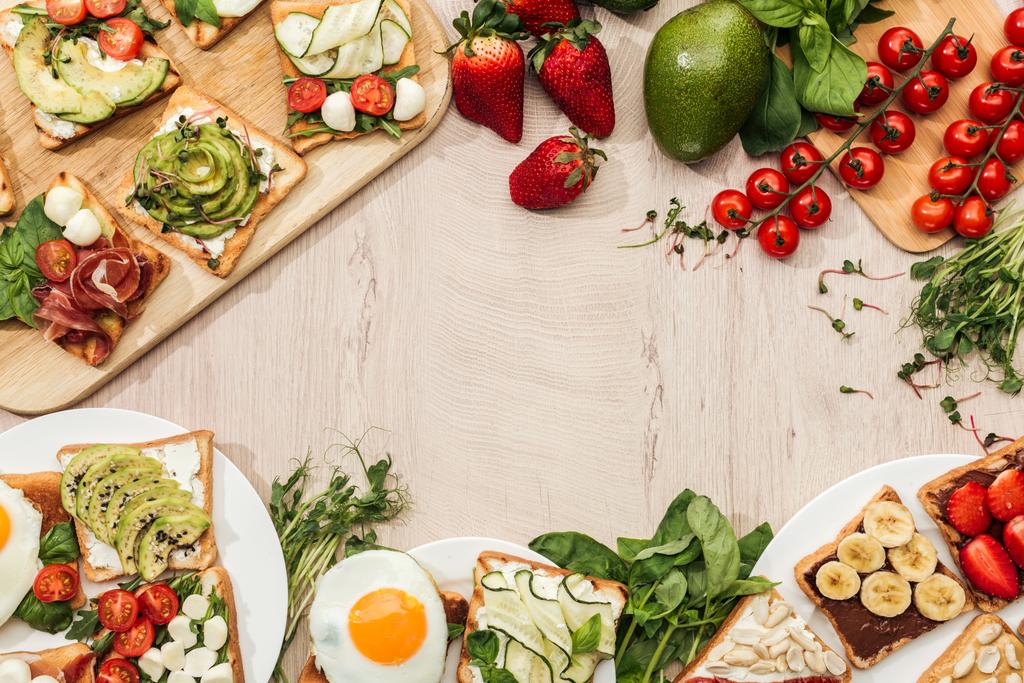 vista superior de tostadas con verduras, frutas y jamón con vegetación e ingredientes en mesa de madera
 - Foto, imagen