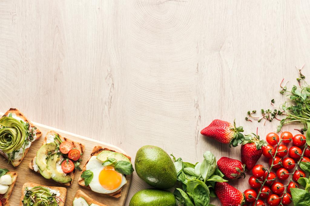 top view of ingredients on wooden table and toasts with vegetables on chopping board - Photo, Image
