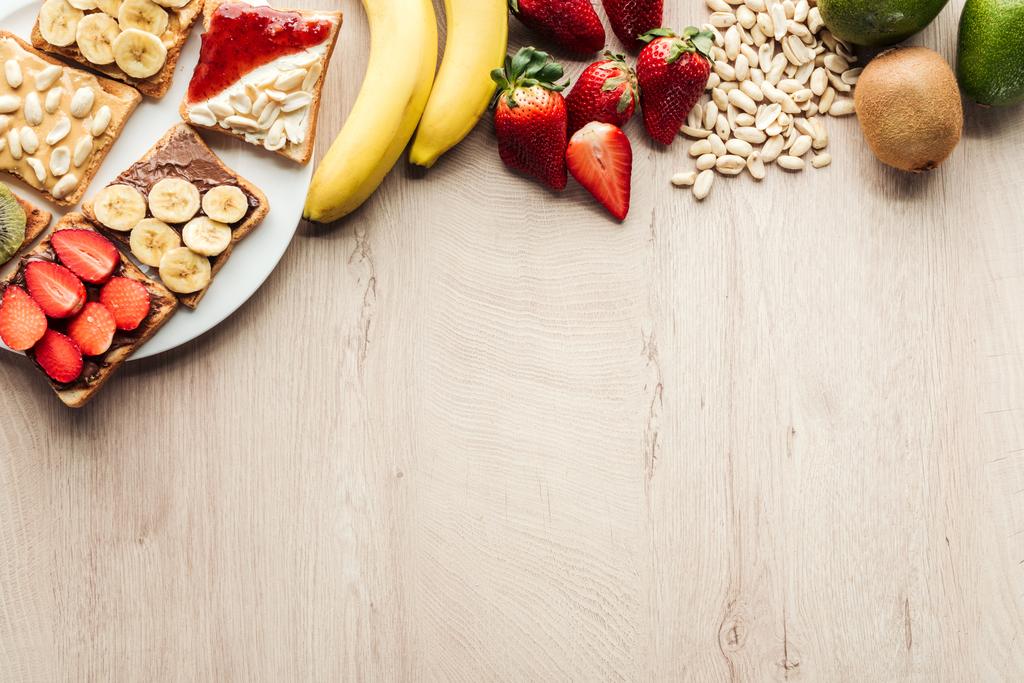 top view of bananas, strawberries, peanuts and toasts on wooden table with copy space - Photo, Image