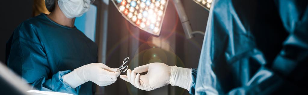 Panoramaaufnahme einer Krankenschwester in Uniform, die dem Chirurgen medizinisches Gerät gibt  - Foto, Bild