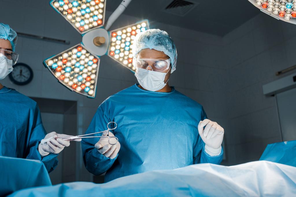 νοσοκόμα και χειρουργός σε στολές και ιατρικές μάσκες που κάνουν τη λειτουργία  - Φωτογραφία, εικόνα