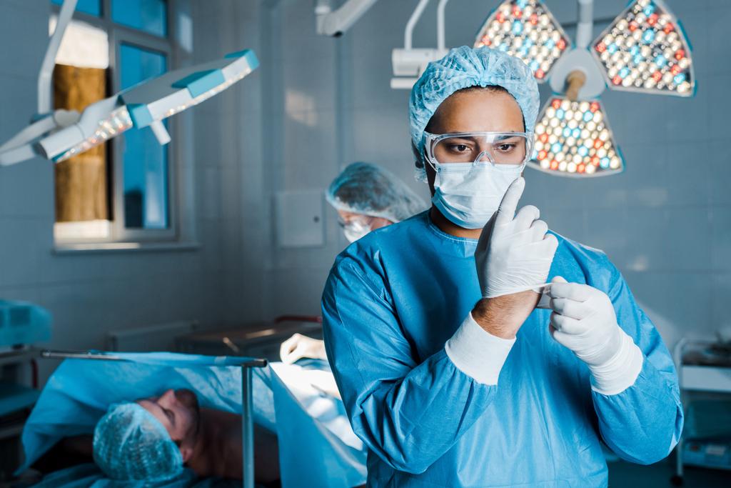 selective focus of doctor in uniform putting off latex gloves in operating room - Photo, Image