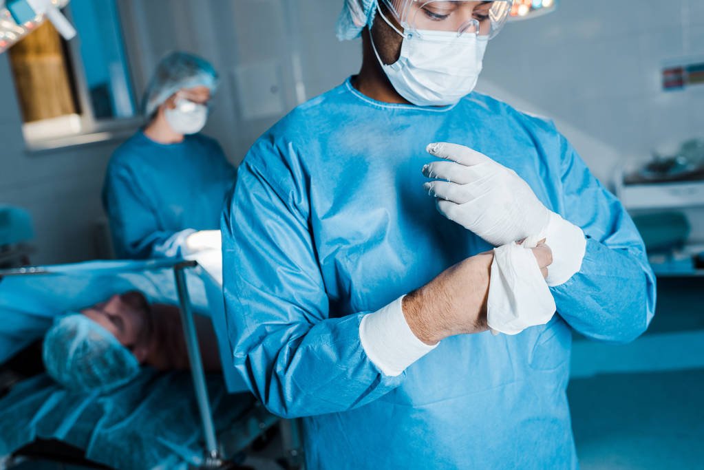 Selektiver Fokus des Arztes in Uniform, der im Operationssaal Latexhandschuhe ablegt - Foto, Bild