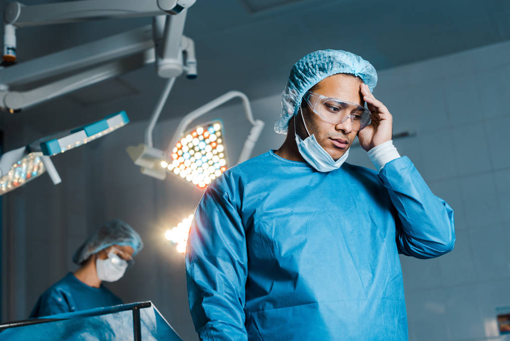 foco seletivo do médico em uniforme e máscara médica olhando para baixo na sala de cirurgia
 - Foto, Imagem