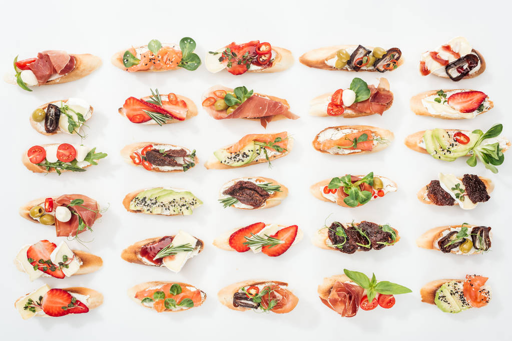 фон італійської брушетта з лососем, прошутто, сушеними помідорами, авокадо, полуницею та травами на білому
 - Фото, зображення