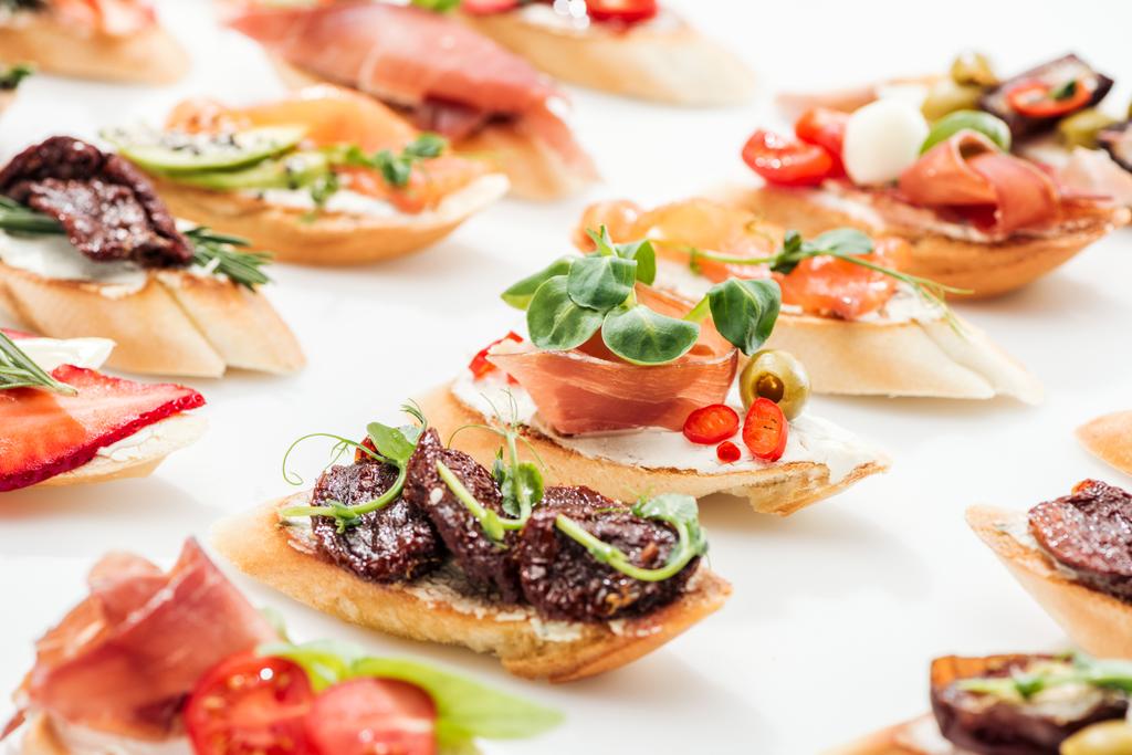 selective focus of italian bruschetta with dried tomatoes, prosciutto and herbs on white - Photo, Image