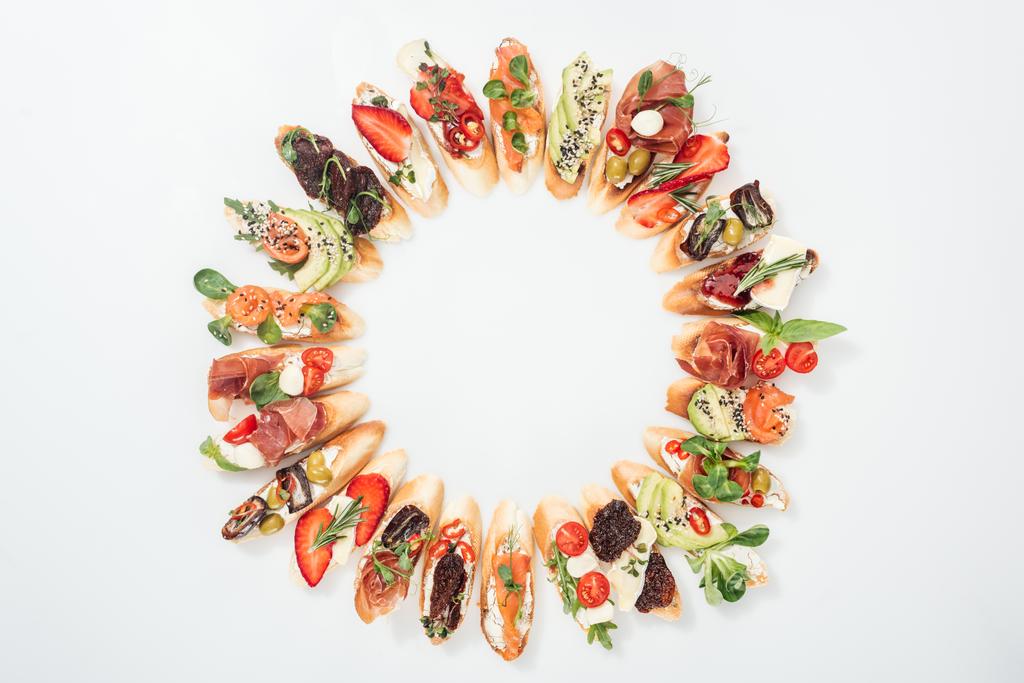 vista superior de marco redondo hecho de deliciosa bruschetta italiana con salmón, jamón, hierbas y varias frutas con verduras
 - Foto, Imagen