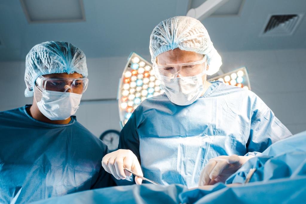 Enfermera y cirujano en uniformes y máscaras médicas operando en quirófano
  - Foto, Imagen