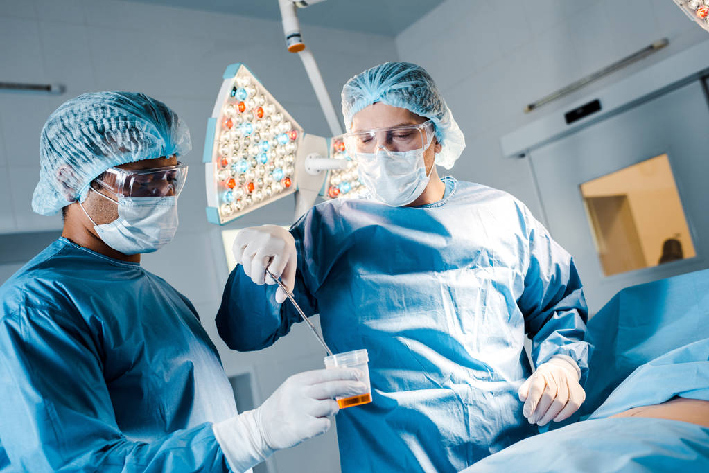 az egyenruhában és az orvosi maszkban működő ápolónő és sebész, műtőben történő üzemeltetés  - Fotó, kép