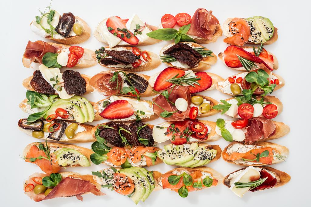 fundo de saborosa bruschetta italiana com salmão, prosciutto, tomates secos, abacate, morangos e ervas em branco
 - Foto, Imagem