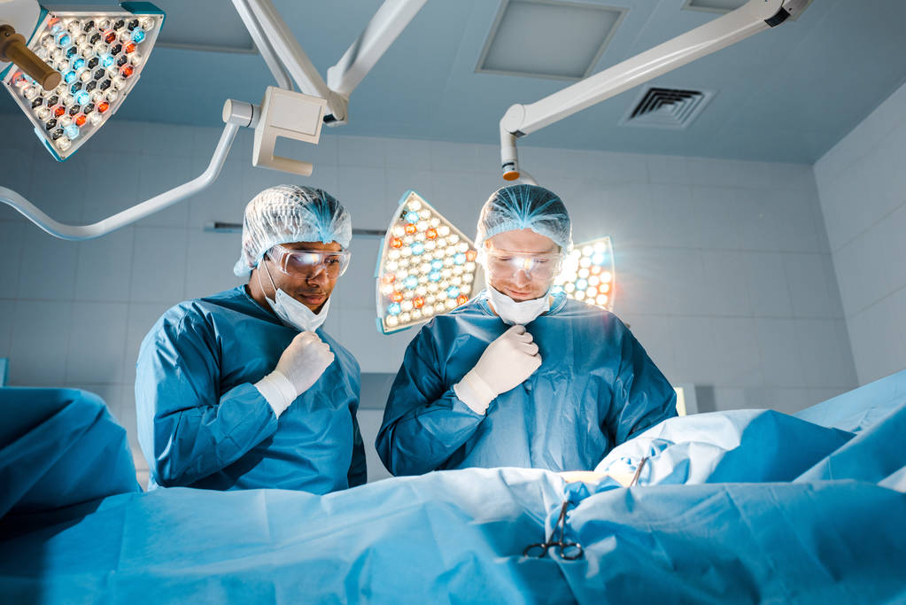 enfermera y cirujano en uniformes que se quitan las máscaras médicas en el quirófano
  - Foto, Imagen