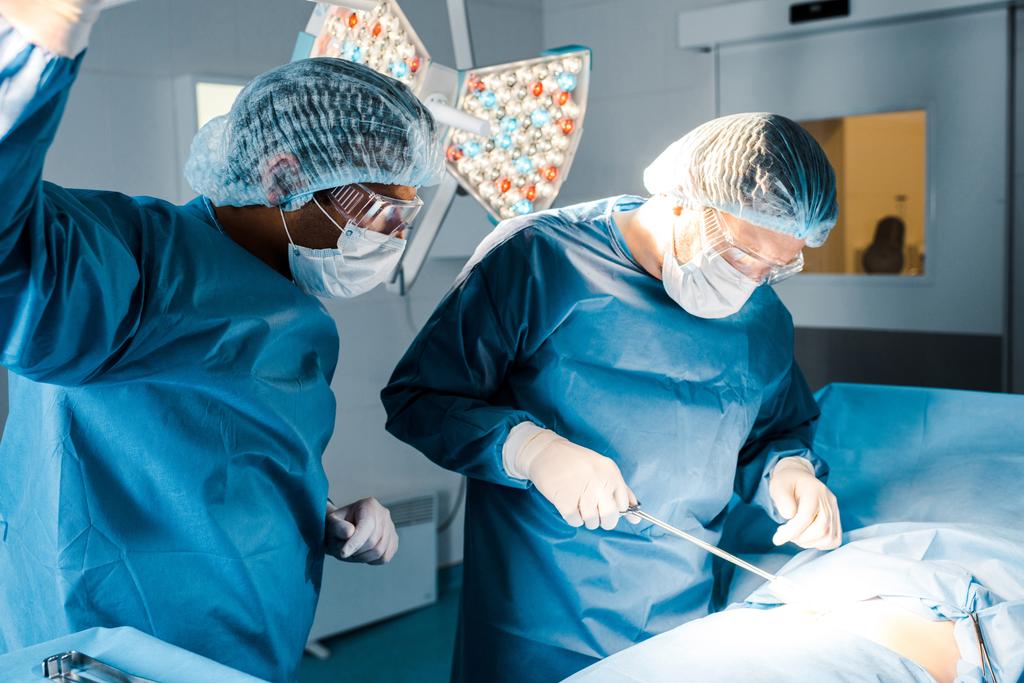 медсестра та хірург в уніформі та медичних масках виконують операцію в операційній кімнаті
  - Фото, зображення